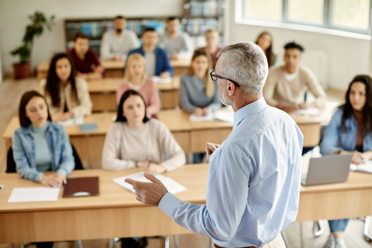 Rear view of mature teacher talking to his student during lecture at university classroom.